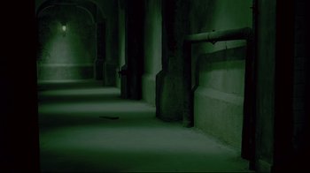Movie still from “Saw 3D” (2010), directed by Kevin Greutert – A dark hallway with pillars and a green light in the background; Wide shot, High angle