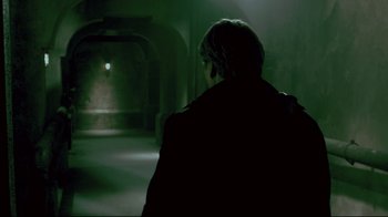 Movie still from “Saw 3D” (2010), directed by Kevin Greutert – A man standing in a dark room looking at the light; Medium shot, Over the shoulder angle