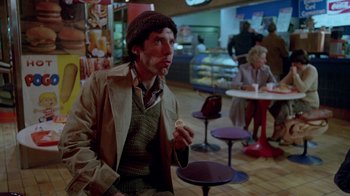 Movie still from “Scanners” (1981), directed by David Cronenberg – A man in a hat and jacket eating a donut; Medium shot, High angle