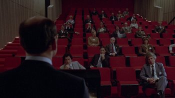 Movie still from “Scanners” (1981), directed by David Cronenberg – A group of people sitting in rows in a theater; Wide shot, High angle
