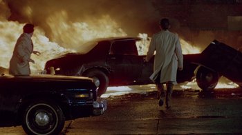 Movie still from “Scanners” (1981), directed by David Cronenberg – A man in a lab coat walking past a car on fire; Wide shot, Low angle