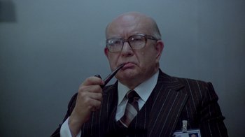Movie still from “Scanners” (1981), directed by David Cronenberg – An older man wearing a suit and tie holding a pipe in his mouth; Close Up shot, Over the shoulder angle