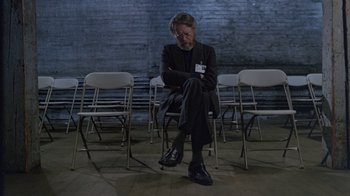Movie still from “Scanners” (1981), directed by David Cronenberg – A man sitting on a chair in front of some chairs; Wide shot, High angle