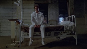 Movie still from “Scanners” (1981), directed by David Cronenberg – A man sitting on top of a bed in a room; Wide shot, Low angle