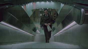 Movie still from “Scanners” (1981), directed by David Cronenberg – A man is walking down the escalator with a bag; Wide shot, High angle