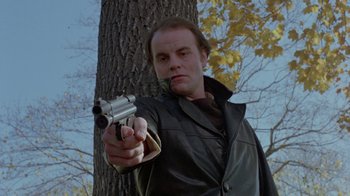 Movie still from “Scanners” (1981), directed by David Cronenberg – A man holding a gun in front of a tree; Medium shot, Low angle
