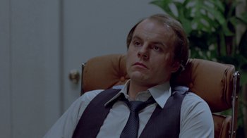 Movie still from “Scanners” (1981), directed by David Cronenberg – A man sitting in an office chair wearing a tie; Close Up shot, Low angle