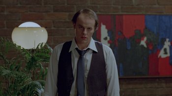 Movie still from “Scanners” (1981), directed by David Cronenberg – A man wearing a vest and tie standing in front of a brick wall; Medium shot, Low angle