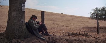 Movie still from “Scarecrow” (1973), directed by Jerry Schatzberg – A man sitting on the side of a dirt road; Wide shot, High angle