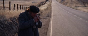 Movie still from “Scarecrow” (1973), directed by Jerry Schatzberg – An older man smoking a cigarette on the side of a road; Wide shot, Over the shoulder angle