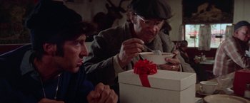 Movie still from “Scarecrow” (1973), directed by Jerry Schatzberg – Two people sitting at a table with a gift; Medium shot, Over the shoulder angle