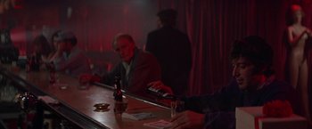Movie still from “Scarecrow” (1973), directed by Jerry Schatzberg – A man sitting at a bar holding a bottle of beer; Medium shot, Over the shoulder angle