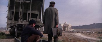 Movie still from “Scarecrow” (1973), directed by Jerry Schatzberg – A man in a hat and a coat holding a suitcase; Wide shot, Low angle