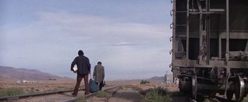 Movie still from “Scarecrow” (1973), directed by Jerry Schatzberg – Two people walking on a dirt road near a tall building; Extreme Wide shot, Low angle