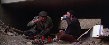 Movie still from “Scarecrow” (1973), directed by Jerry Schatzberg – Two men sitting on the ground drinking from cups; Wide shot, Low angle