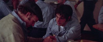 Movie still from “Scarecrow” (1973), directed by Jerry Schatzberg – A man sitting at a table with another man in the background; Close Up shot, Over the shoulder angle