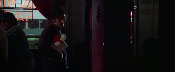 Movie still from “Scarecrow” (1973), directed by Jerry Schatzberg – A man holding a box of presents in a dark room; Medium shot, Over the shoulder angle