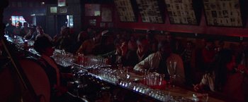 Movie still from “Scarecrow” (1973), directed by Jerry Schatzberg – A group of people sitting at a bar with drinks on the counter; Wide shot, Over the shoulder angle