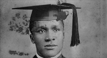 Movie still from “School Daze” (1988), directed by Spike Lee – An old black and white photo of a man wearing a graduation cap; Extreme Close Up shot, Low angle