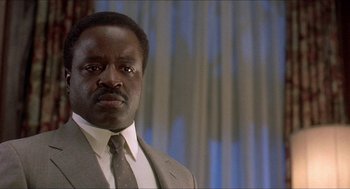 Movie still from “School Daze” (1988), directed by Spike Lee – A man wearing a suit and tie in front of a curtain; Close Up shot, Low angle