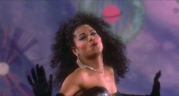 Movie still from “School Daze” (1988), directed by Spike Lee – A woman in a black dress with long black curly hair; Close Up shot, Low angle