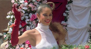Movie still from “School Daze” (1988), directed by Spike Lee – A woman in a white top and a bunch of pink flowers; Medium shot, Low angle