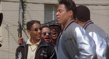 Movie still from “School Daze” (1988), directed by Spike Lee – A group of men standing next to each other on a street; Medium shot, Low angle