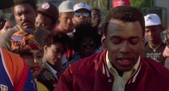 Movie still from “School Daze” (1988), directed by Spike Lee – A group of people standing in a line with a man in a red jacket; Close Up shot, Over the shoulder angle