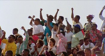 Movie still from “School Daze” (1988), directed by Spike Lee – A group of people standing in a stadium with their hands raised; Extreme Wide shot, High angle