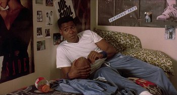 Movie still from “School Daze” (1988), directed by Spike Lee – A man sitting on a bed holding a football; Medium shot, High angle