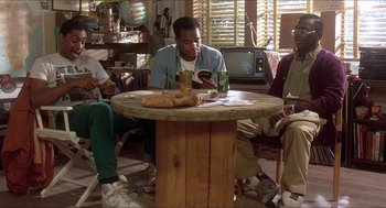 Movie still from “School Daze” (1988), directed by Spike Lee – A man sitting at a wooden table with a sandwich; Wide shot, High angle