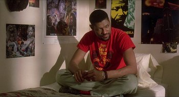 Movie still from “School Daze” (1988), directed by Spike Lee – A man sitting on the ground in a room; Medium shot, Over the shoulder angle
