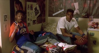 Movie still from “School Daze” (1988), directed by Spike Lee – Two young men sitting on a couch in a room; Wide shot, High angle