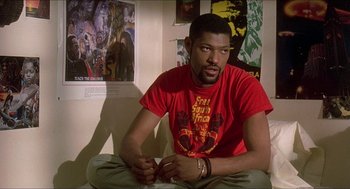 Movie still from “School Daze” (1988), directed by Spike Lee – A man sitting on the ground in front of a wall; Medium shot, Over the shoulder angle