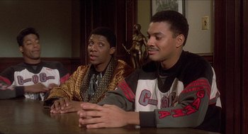 Movie still from “School Daze” (1988), directed by Spike Lee – Two young men sitting at a table in front of a statue; Medium shot, Over the shoulder angle