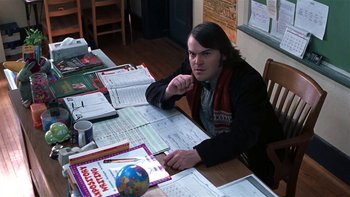 Movie still from “School of Rock” (2003), directed by Richard Linklater – A man sitting at a table with papers on it; Medium shot, High angle