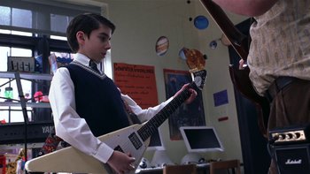 Movie still from “School of Rock” (2003), directed by Richard Linklater – A young man holding a white guitar in a room; Medium shot, Low angle