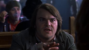Movie still from “School of Rock” (2003), directed by Richard Linklater – A man with long brown hair is sitting in front of some people; Close Up shot, Over the shoulder angle