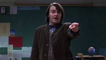 Movie still from “School of Rock” (2003), directed by Richard Linklater – A man in a brown jacket and a tie points to something; Medium shot, Over the shoulder angle