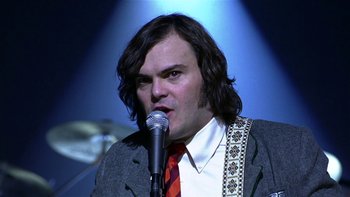 Movie still from “School of Rock” (2003), directed by Richard Linklater – A man with long black hair wearing a suit and red tie; Close Up shot, Low angle