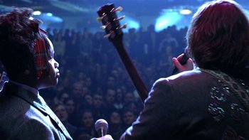 Movie still from “School of Rock” (2003), directed by Richard Linklater – A man holding a guitar in front of an audience; Medium shot, Low angle
