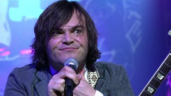 Movie still from “School of Rock” (2003), directed by Richard Linklater – A man holding a microphone while wearing a suit; Close Up shot, Low angle