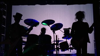 Movie still from “School of Rock” (2003), directed by Richard Linklater – A group of people that are sitting around a drum set; Wide shot, Low angle