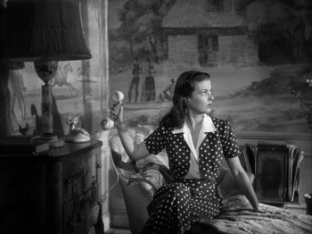 Movie still from “Secret Beyond the Door...” (1947), directed by Fritz Lang – A black and white photo of a woman sitting on a couch holding a phone; Medium shot, Low angle