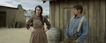 Movie still from “Godless” (2017), directed by Scott Frank – A man and a woman standing next to each other in front of a barrel; Medium shot, Over the shoulder angle