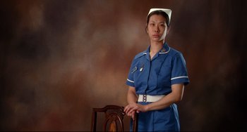Movie still from “Secrets & Lies” (1996), directed by Mike Leigh – A woman in a nurse's uniform standing in front of a chair; Medium shot, Low angle