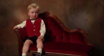 Movie still from “Secrets & Lies” (1996), directed by Mike Leigh – A little boy sitting on top of a red couch; Medium shot, High angle