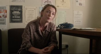 Movie still from “Secrets & Lies” (1996), directed by Mike Leigh – A woman sitting at a desk in front of papers; Medium shot, Low angle