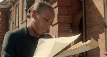 Movie still from “Secrets & Lies” (1996), directed by Mike Leigh – A woman looking at a piece of paper in front of a brick building; Close Up shot, Low angle