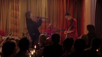Movie still from “Serendipity” (2001), directed by Peter Chelsom – A group of people playing instruments in front of an audience; Wide shot, Over the shoulder angle
